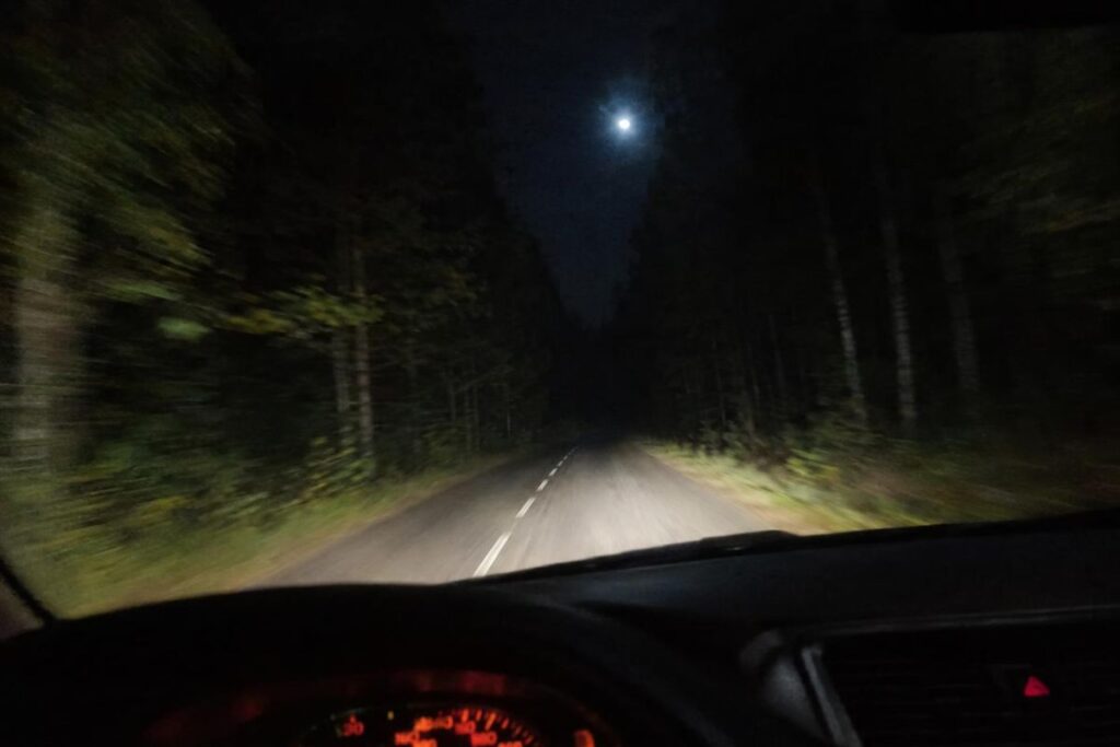 Route forestière de nuit éclairée par des phares, lumière vive au-dessus des arbres