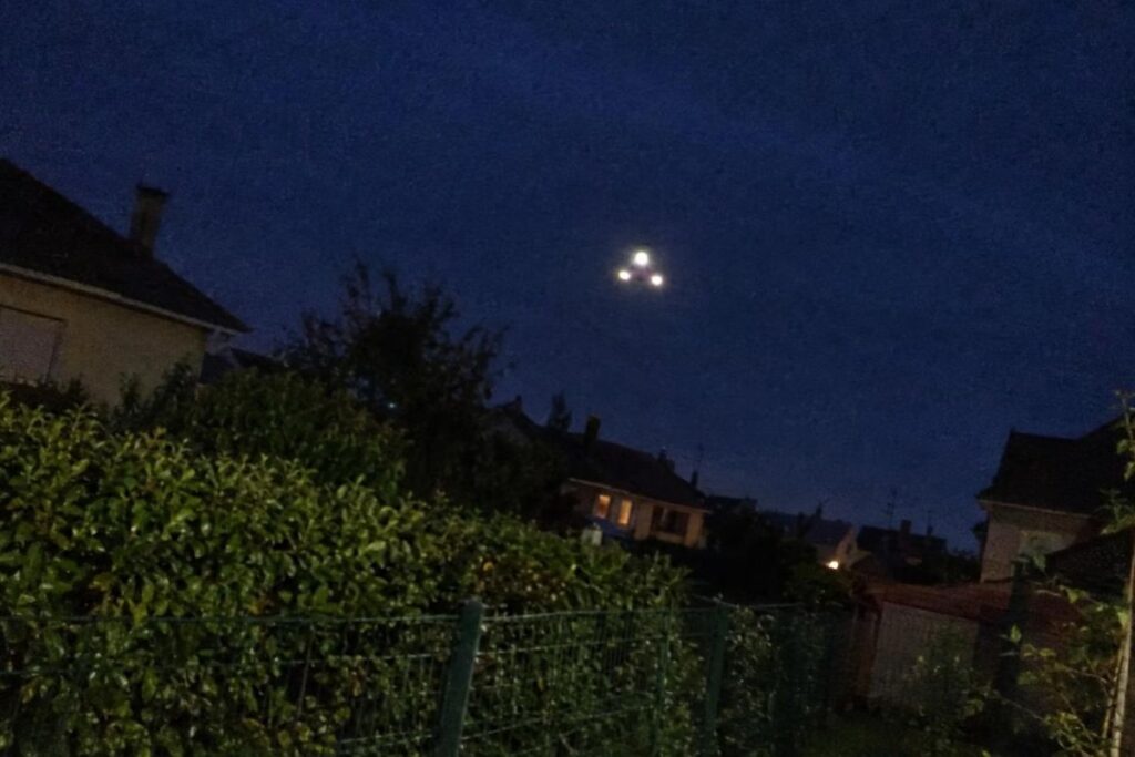 Trois lumières immobiles dans le ciel du soir au-dessus d’un jardin