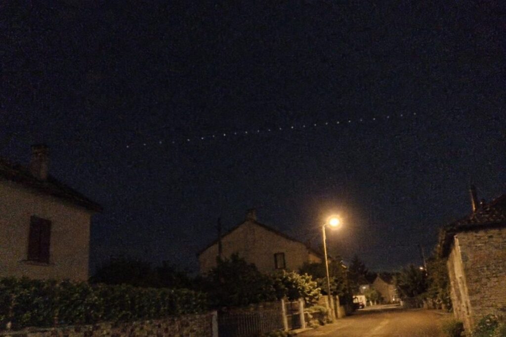 Train de satellites Starlink alignés dans le ciel nocturne au-dessus d’un village