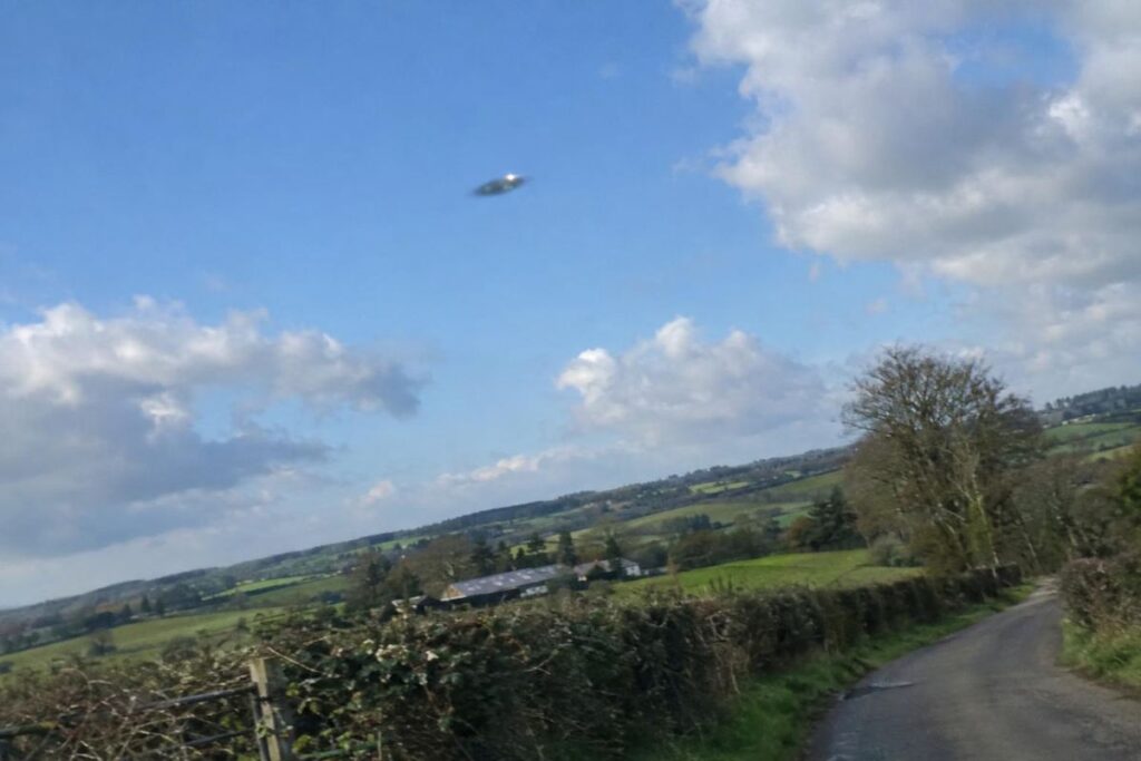 Illustration : objet discoïde métallique dans un ciel de jour au-dessus de la campagne