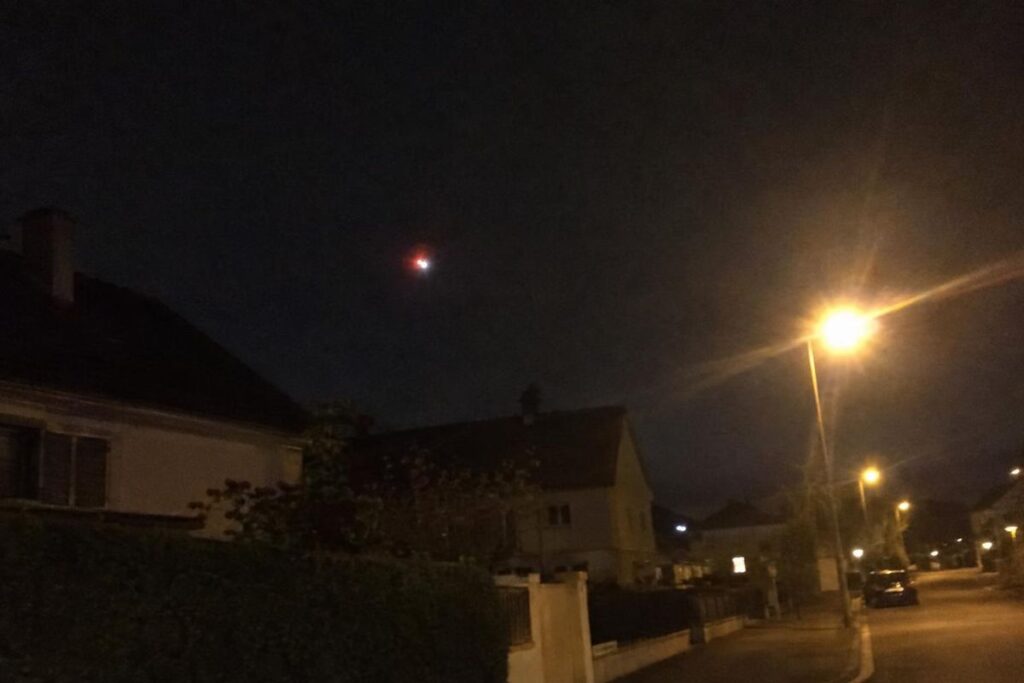 Illustration : lumière rouge dans le ciel au-dessus d’une rue de quartier